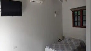 Ein Zimmer mit einem Bett, einem an der Wand befestigten Fernseher und einem Fenster mit Holzrahmen.