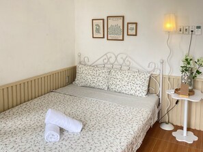 Una cama bien hecha con ropa de cama floral, una toalla enrollada y un cuadro en la pared.