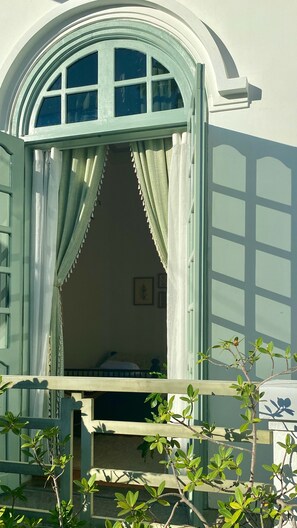 Una habitación con ventana, cortinas, una cama y una pequeña planta.