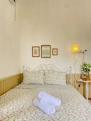 Una cama con ropa de cama floral, cabecera de metal blanco y dos toallas enrolladas.