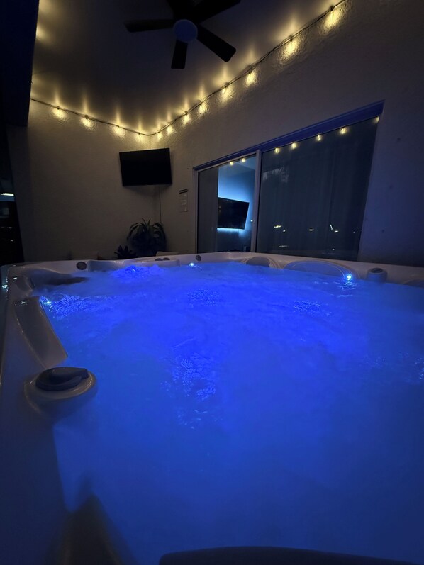 A hot tub with blue lighting, a ceiling fan, and a TV mounted on the wall.