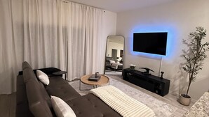 Uma sala de estar moderna com um sofá, uma mesa de centro, uma TV, um ventilador de teto e um vaso com planta.