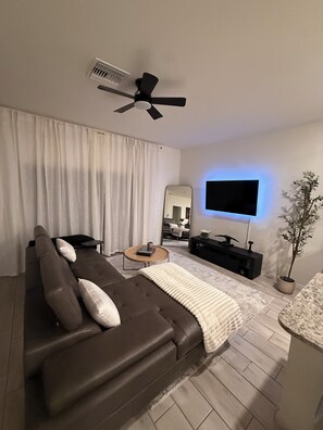 Una sala de estar moderna con un sofá, una mesa de centro, un televisor, un ventilador de techo y una planta en maceta.