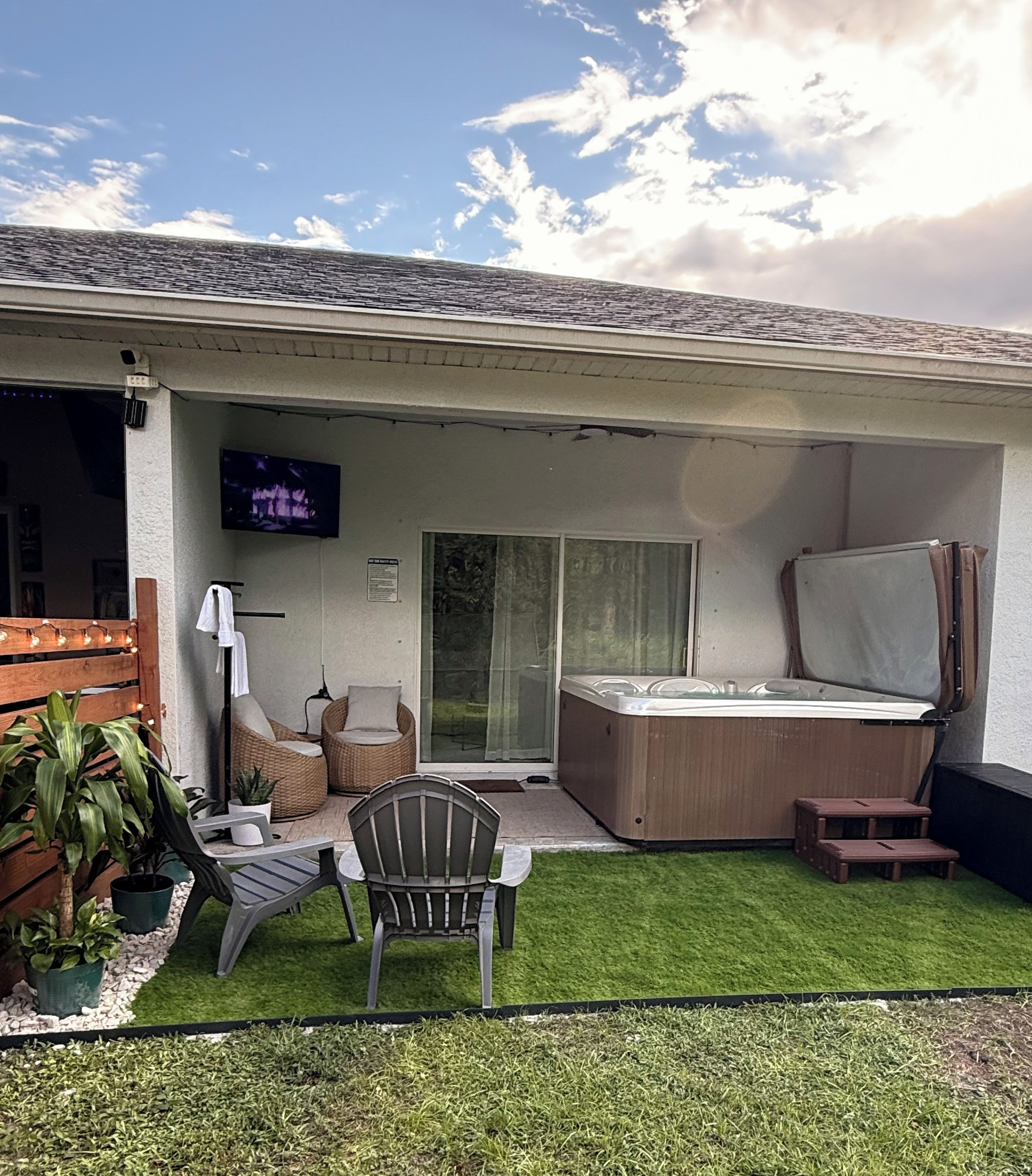 A covered patio area with a hot tub, outdoor seating, and a television screen.