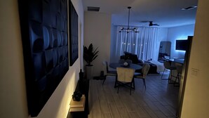 Uma sala de estar moderna com área de jantar, uma grande pintura abstrata e um ventilador de teto.