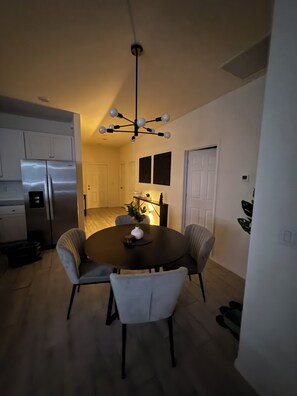 Una cocina compacta con un refrigerador moderno, una mesa de comedor con cuatro sillas y una lámpara colgante.