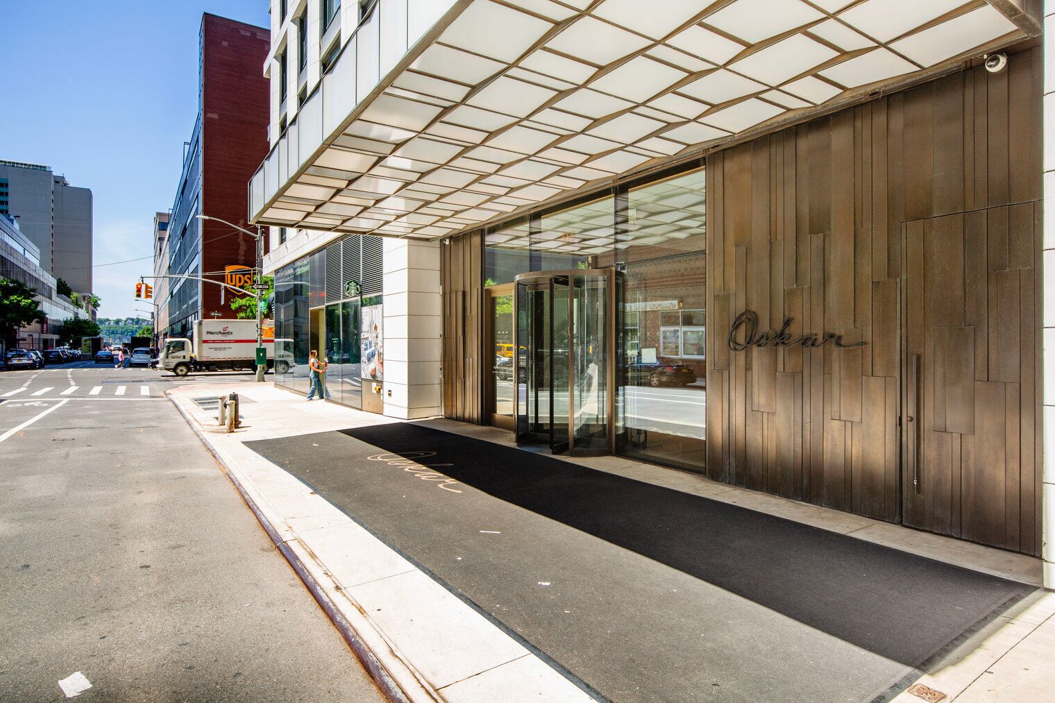 Ein moderner Hotel Eingang mit Glasfassade, einer Holzwand mit dem Schriftzug 'Oaks' und einem UPS-Wagen, der draußen geparkt ist.