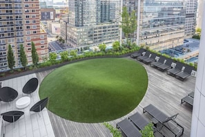 Eine Dachterrasse mit einem runden Rasen, Liegestühlen und Blick auf die Stadtlandschaft.