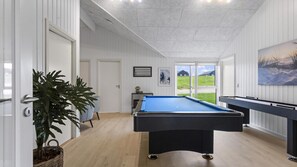 Ein Billardtisch in einem Raum mit weißen Wänden, Holzboden und einer Tür, die auf einen Balkon mit Blick führt.