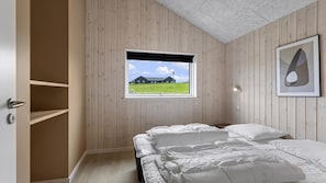 Ein Schlafzimmer mit Bett, Fenster mit Blick auf ein Haus, einem Regal und einem gerahmten Bild an der Wand.