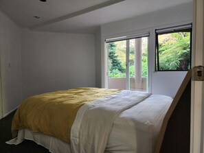 A bedroom with a bed, a window with a view of greenery, and a door. - Entire Ground-floor: Spacious 145m2 (Auckland)