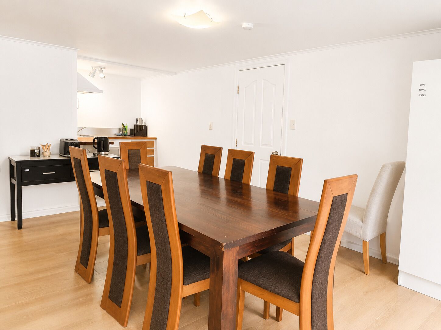 A dining area with a wooden table and chairs, a kitchen area with a stove and cabinets, and a white door.