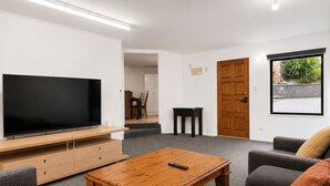 Olohuoneessa on taulutelevisio, puinen sohvapöytä, harmaa sohva ja ovi, joka johtaa parvekkeelle, jolta on näkymä vehreään maisemaan.