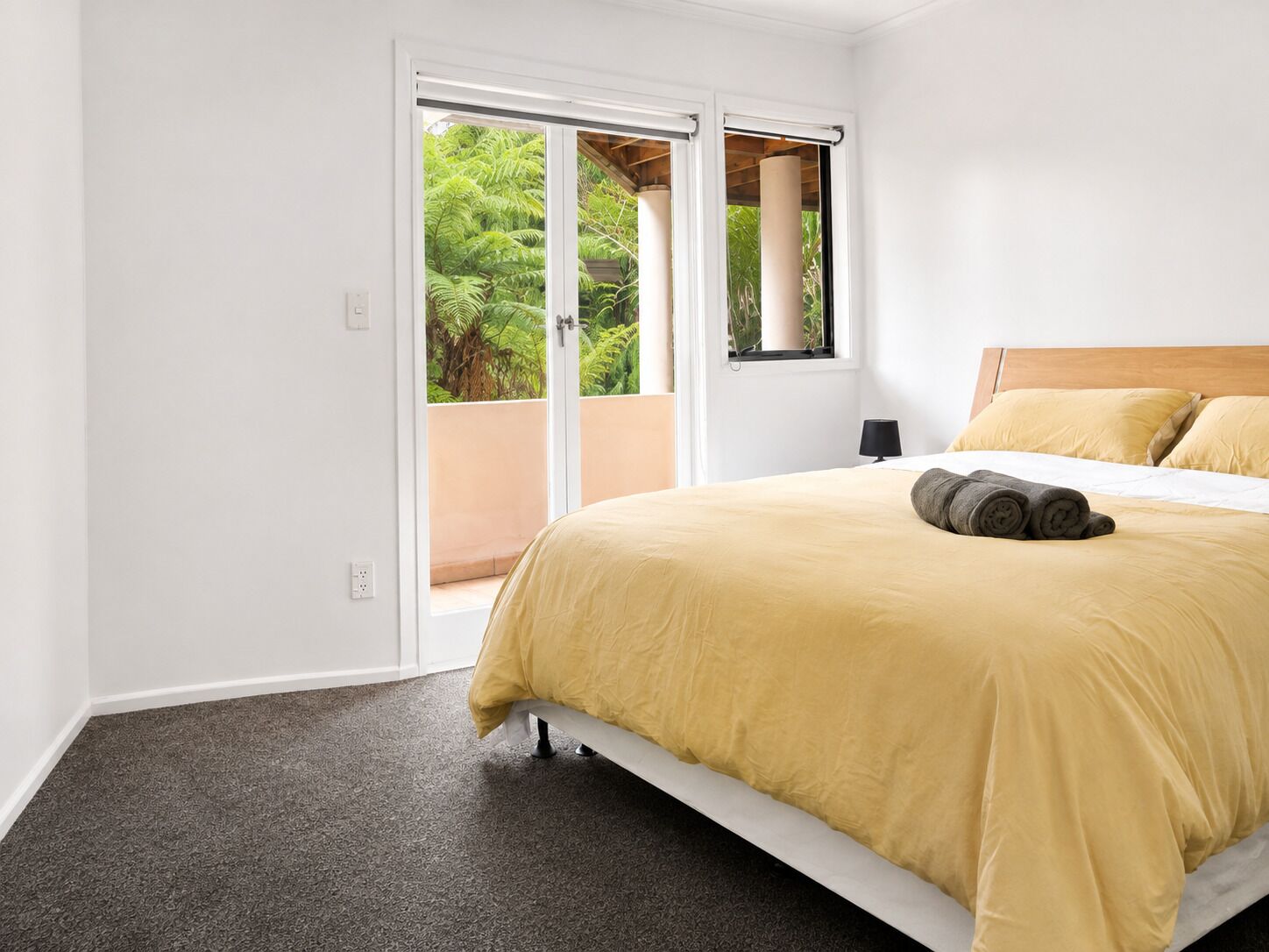 A hotel room with a bed, a window, and a view of greenery outside.