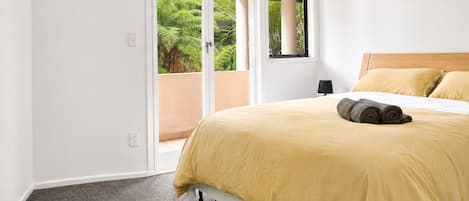 A hotel room with a bed, a window, and a view of greenery outside.