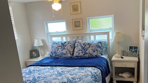 A bedroom with a bed, a nightstand, a lamp, a ceiling fan, and a window.