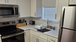 A modern kitchen with white cabinets, stainless steel appliances, and a wooden floor.