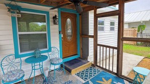 A covered porch with a ceiling fan, a wooden door, and a view of a house in the background.