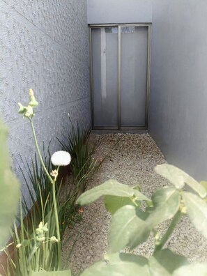 A narrow outdoor corridor with a textured wall, a metal door, and gravel flooring. - Beautiful home just 6 minutes from the heart of Oaxaca City (Oaxaca de Juárez)