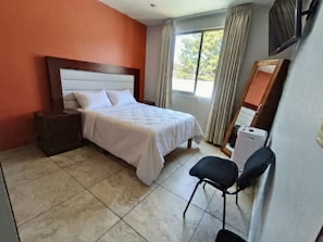 Ein Hotelzimmer mit Bett, Schreibtisch, Stuhl, Fernseher und einem Fenster mit Vorhängen.
