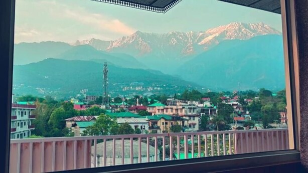 A view of a town with mountains in the background, a tall communication tower, and buildings with green roofs. - Asian resort n farm  (Dharamshala)