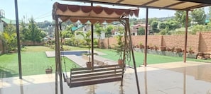 Ein überdachter Patio-Bereich mit Schaukelset, kleinem Pool und Rasenfläche.