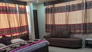 Um quarto com cama, sofá, uma mesinha e cortinas.