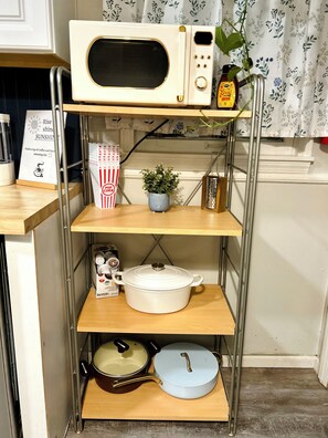 Une cuisine Ă©quipĂ©e dâun four Ă micro-ondes, dâune machine Ă cafĂ©, dâune casserole et dâune plante posĂ©e sur une Ă©tagĂšre.