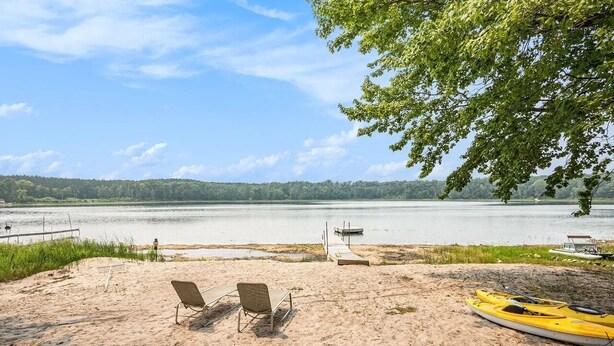 A beach with two lounge chairs, a kayak, and a dock extending into a lake. - Cozy 2-bedroom cottage in Bitely perfect for a relaxing getaway. (Bitely)