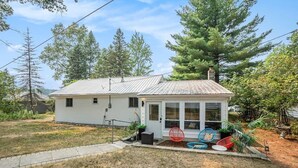 A single-story house with a metal roof, a front porch with a sliding glass door, and a small garden area with outdoor seating. - Cozy 2-bedroom cottage in Bitely perfect for a relaxing getaway. (Bitely)