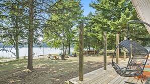 A wooden deck with a hanging chair, a picnic table, and a view of a lake. - Cozy 2-bedroom cottage in Bitely perfect for a relaxing getaway. (Bitely)