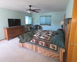 Ein Schlafzimmer mit einem Bett, einem Schminktisch, einem Deckenventilator, einem Fernseher und einem Fenster.