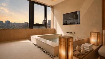 A modern bathroom with a large bathtub, a sink, and a mirror. There is a city view through large windows.