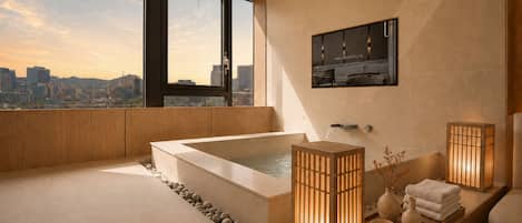 Un baño moderno con una bañera grande, un lavamanos y un espejo. Se observa una vista panorámica de la ciudad a través de amplios ventanales.