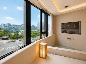 Un baño moderno con bañera, una ventana con vistas a la ciudad y un espejo instalado en la pared.