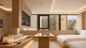 A modern hotel room with a large window, a bed, a seating area, and a small table with a vase and cups.