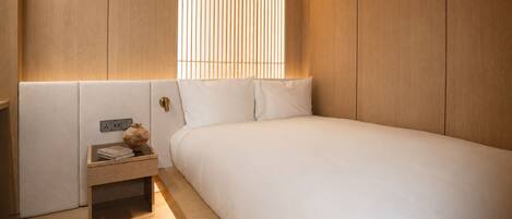 A bedroom with a bed, bedside table, and a window with vertical blinds.