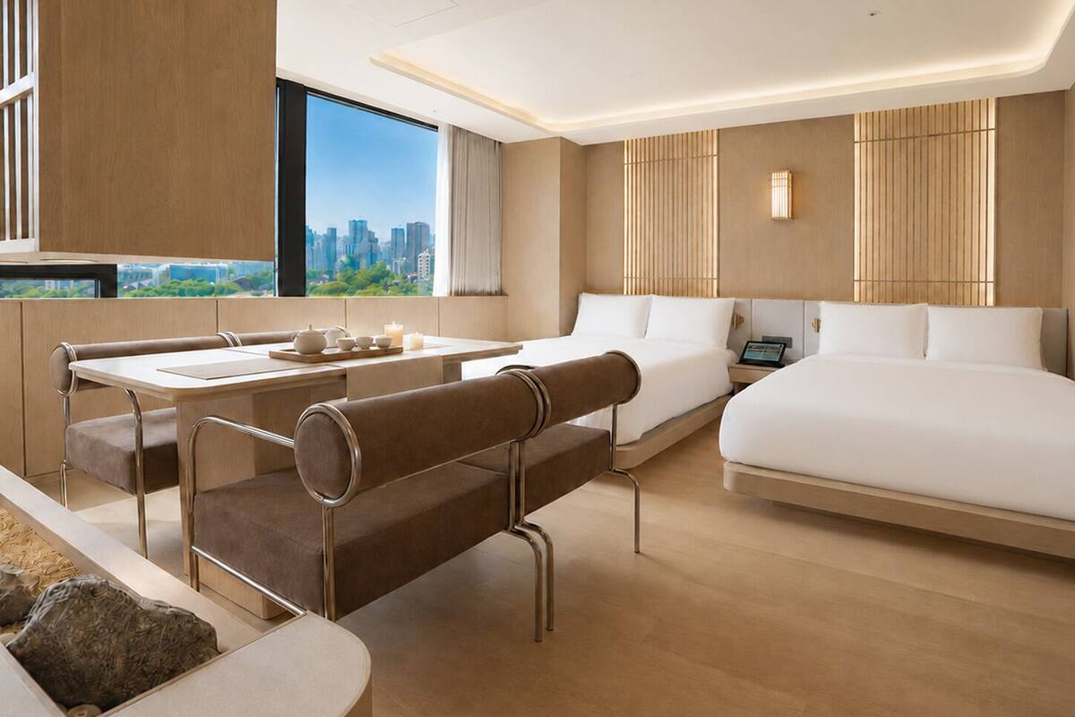 A modern hotel room with a city view, a dining area, and a large bed.