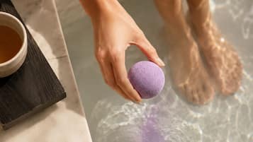 Una mano sostiene una esponja morada sobre una bañera, con una taza de té a un lado.