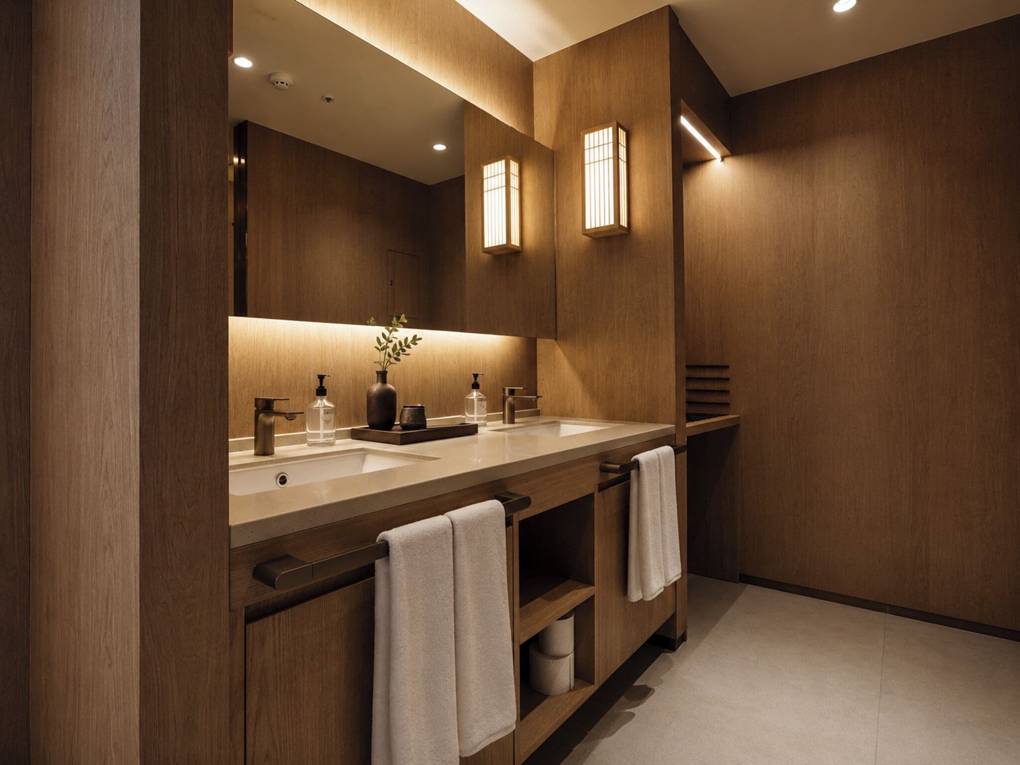 Un baño moderno con paneles de madera, lavamanos doble y un espejo grande.