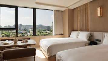 Habitación de hotel con dos camas, una mesa de comedor y vista a un paisaje urbano.