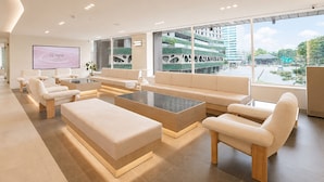 A modern hotel lobby with a large seating area, a flat-screen TV, and a view of the cityscape.
