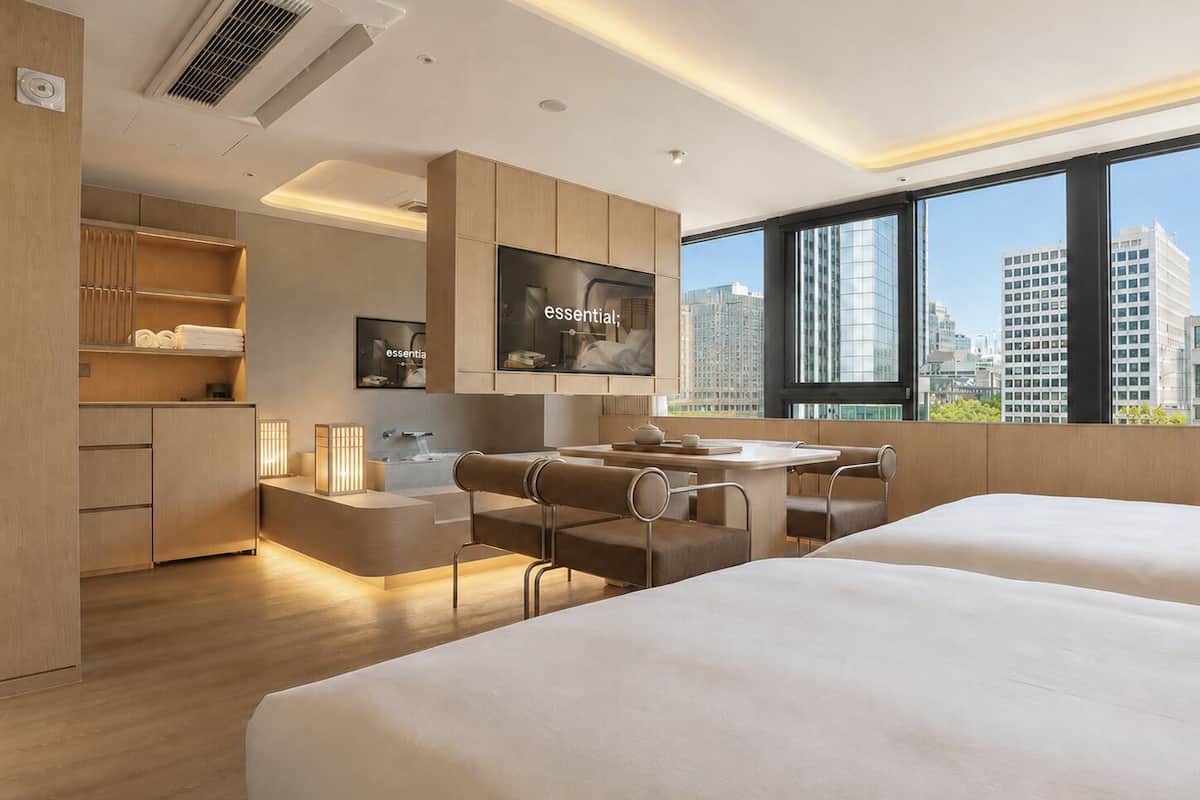 A modern hotel room with a city view, a kitchenette, a seating area, and a large bed.