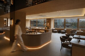 Un interior moderno con una recepción, zona de estar y amplios ventanales con vistas a la ciudad.