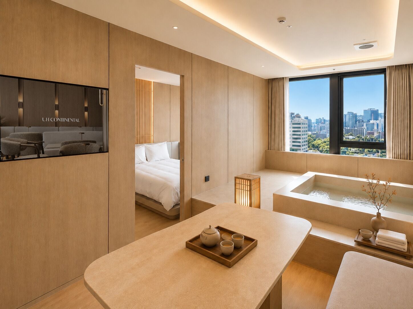 Una habitación de hotel moderna con una cama, un rincón de descanso con una bandeja de té, una bañera y vistas a la ciudad a través de amplios ventanales.