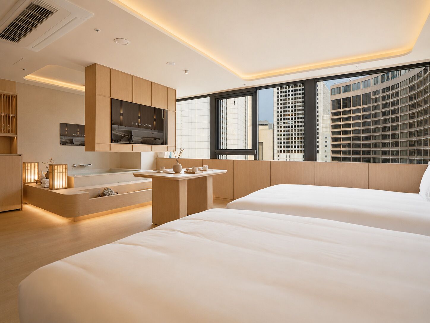 A modern hotel room with a large bed, a small sitting area, a vanity with a mirror, and a view of a cityscape.