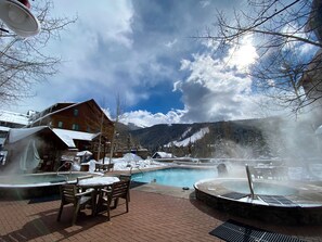 A pool area with a hot tub, outdoor seating, and a view of mountains.