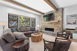 A modern living room with a stone fireplace, large windows, and a cozy seating area.
