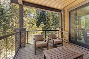 A wooden deck with two chairs and a table, overlooking a forested area.
