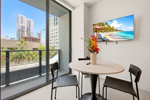 Ein Balkon mit Blick auf die Stadt, ein runder Tisch mit Stühlen, eine Vase mit Blumen und ein Gemälde mit Strandmotiv.